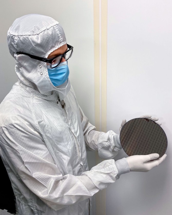Man in full body protective suit holds wafer.
