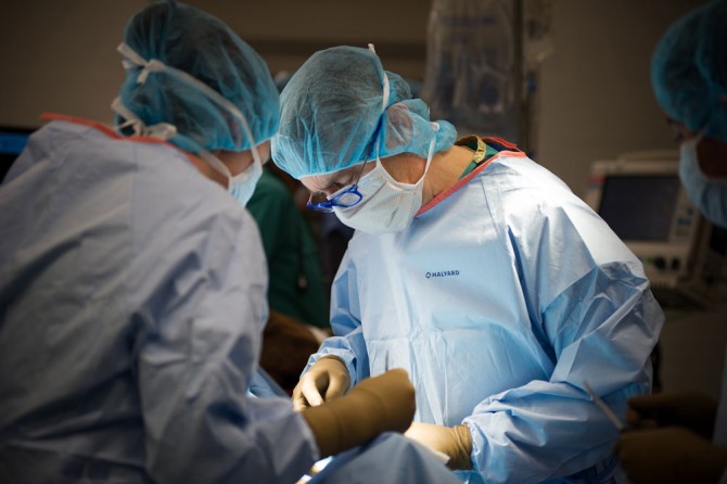 Norm Ducharme in surgery, wearing cap, glasses, mask, scrubs and gloves