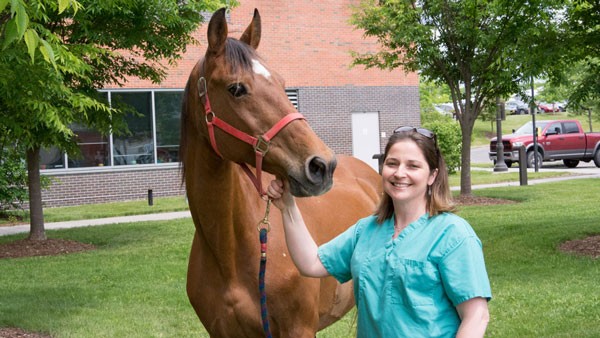 Michelle Delco in scrubs stands next to a horse outside the College of Veterinary Medicine