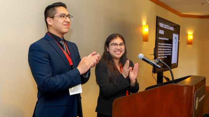 Two students stand at a podium and clap.