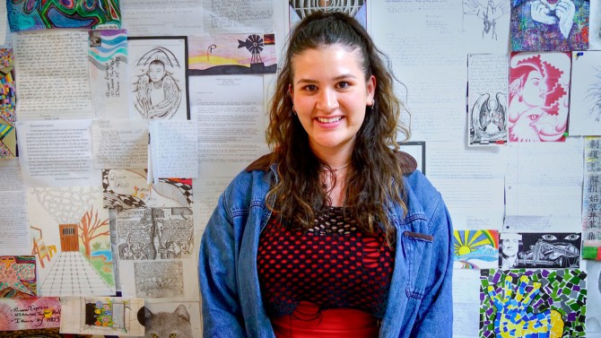 ILR School student and Prisoner Express program volunteer Caroline Apodaca ’25 stands at Durland Alternatives Library in front of art works by incarcerated individuals.