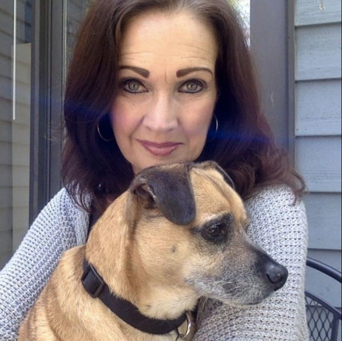 Susan Engelmore, a woman with dark hair wearing a purple sweater, holds Milo, a terrier mix, close to her chest