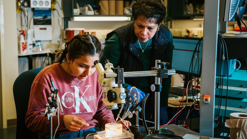 Shivaun Archer guides a student sitting at a microscope in a lab experiment 