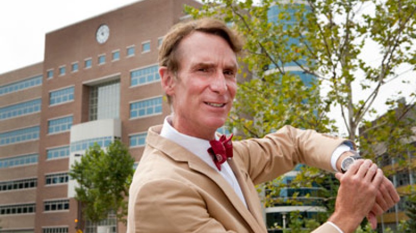Bill Nye looking at his watch outside Rhodes Hall