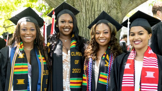 Four graduates smile in the Arts Quad.