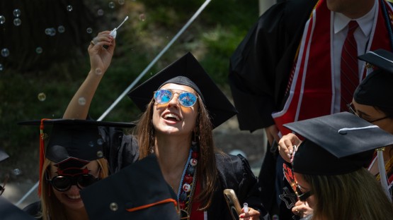 A graduate blows bubbles with a wand.