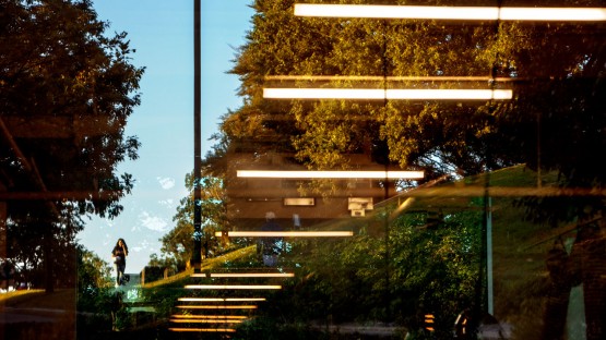 A student is seen walking through campus in a reflection of a Rand Hall window.  