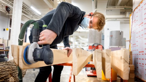 A student sands wood planks in Rand Hall.