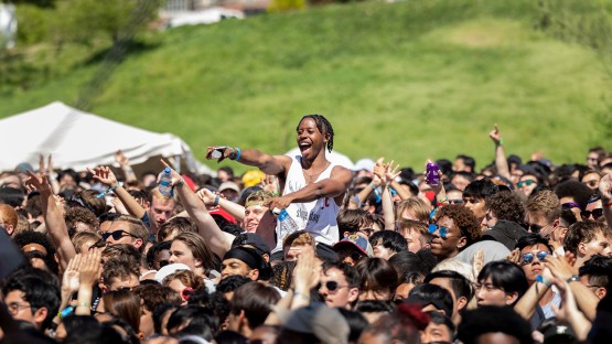 A man on someone's shoulders in the crowd points toward the performers. 
