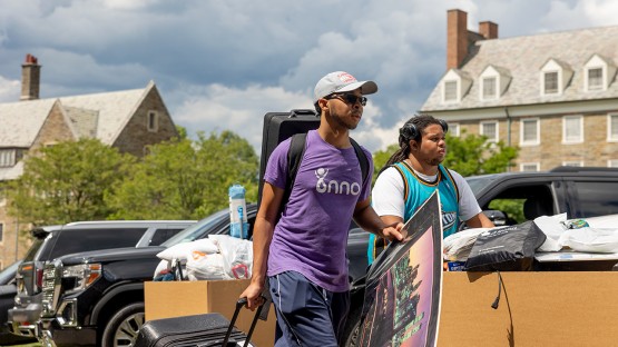 Two students carry their belongings outside a residence hall. 