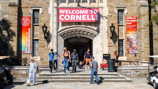 Families on the steps of Willard Straight Hall under a 'Welcome to Cornell' banner. 