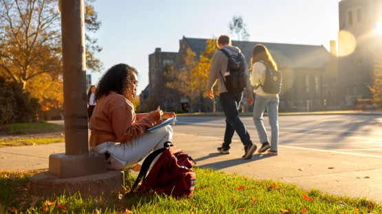 A student studies along College Avenue while waiting for a bus.