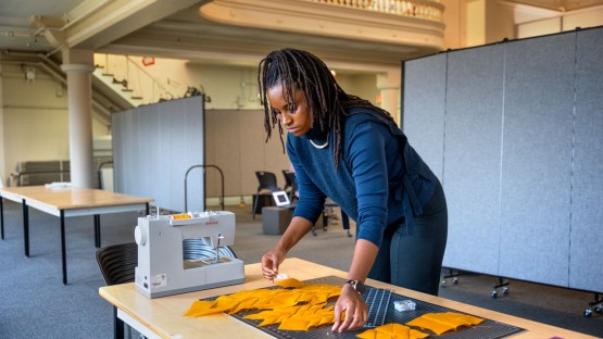 Woman lays out pieces of yellow fabric on table, near sewing machine