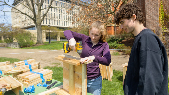 Two people build wooden trusses on Ho Plaza