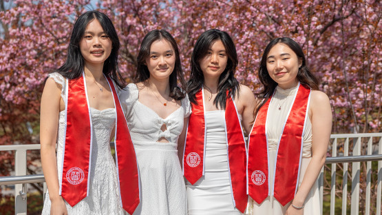 Four students wearing white pose for photos in front of pink flowering trees