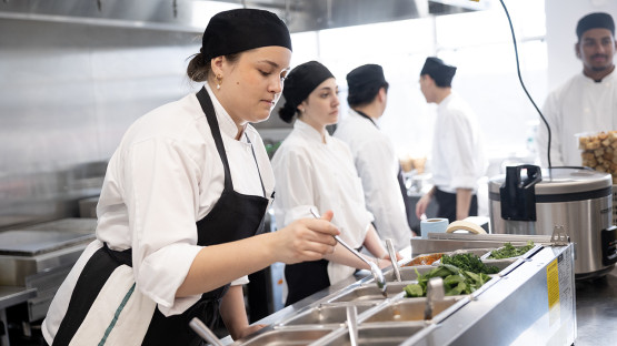 Students work at food prep stations in a commercial kitchen