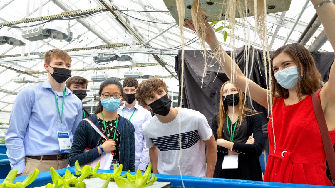Francine Barchett MPS ’21 Ph.D. ’24, far right, and Joseph Tornabene, middle, a student at Clean Technologies & Sustainable Industries Early College High School, inspect an aquaponic system at the Kenneth Post Laboratory greenhouses.