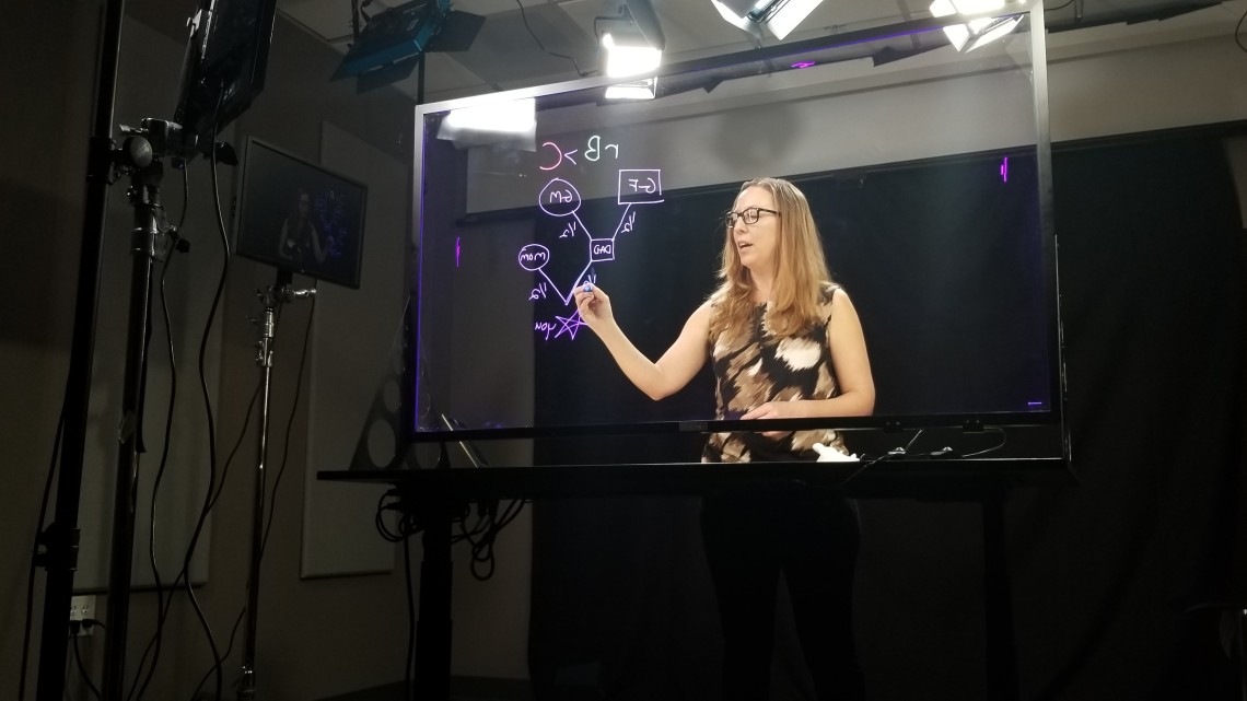 A professor writes equations on a light board
