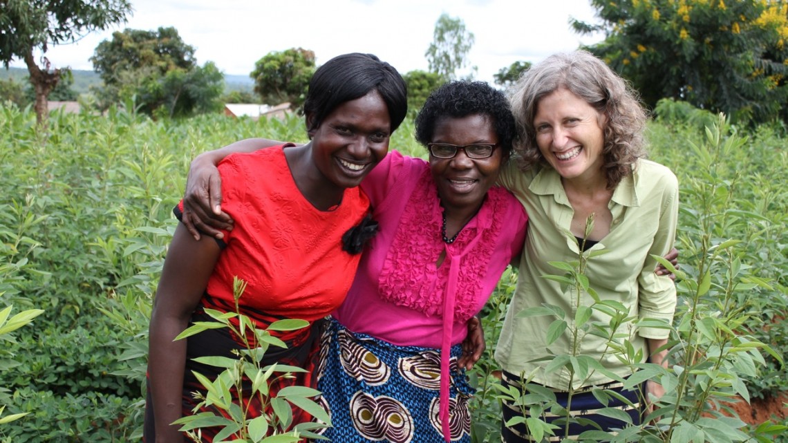 three women stand in a field and smile