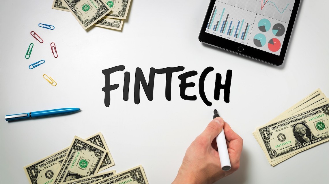 Hand writes "FINTECH" surrounded by money, a chart, and office supplies