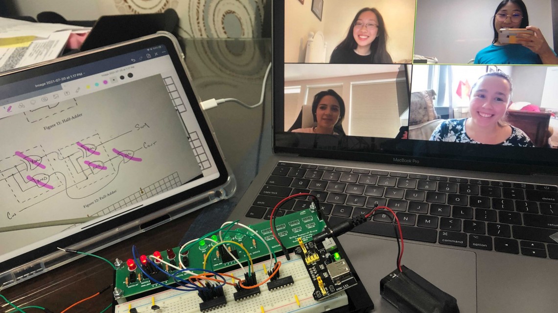 Video chat on a laptop is seen with a circuit board and a design sketch on a table