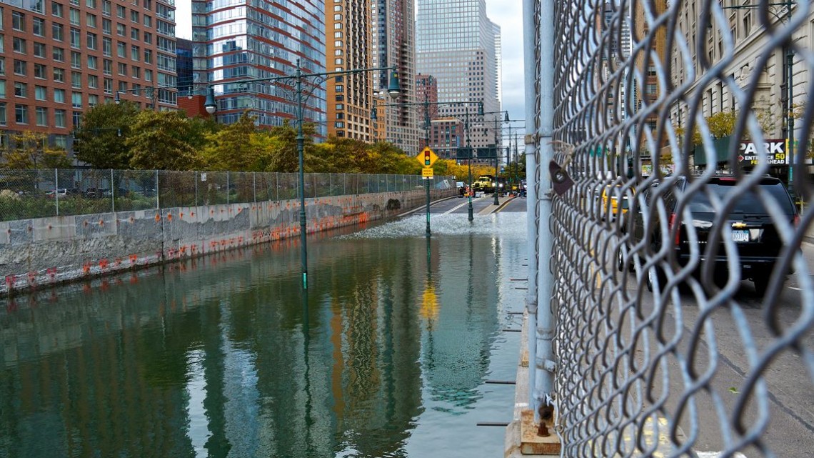 flooded street with chain link fence and skyscrapers background
