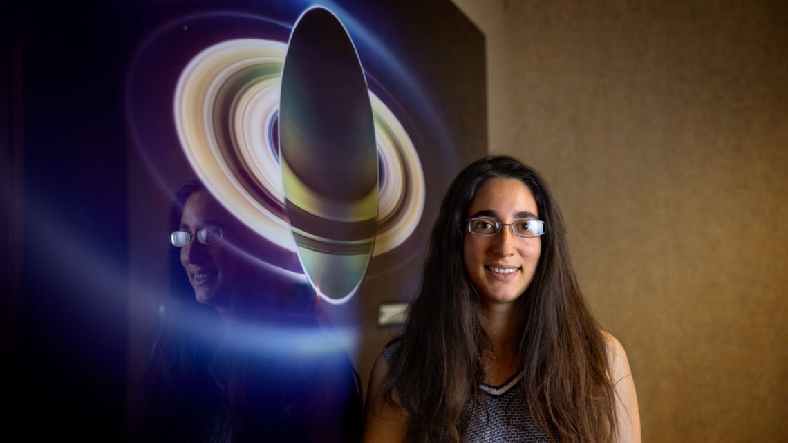 Woman stands in front of photo of Saturn.