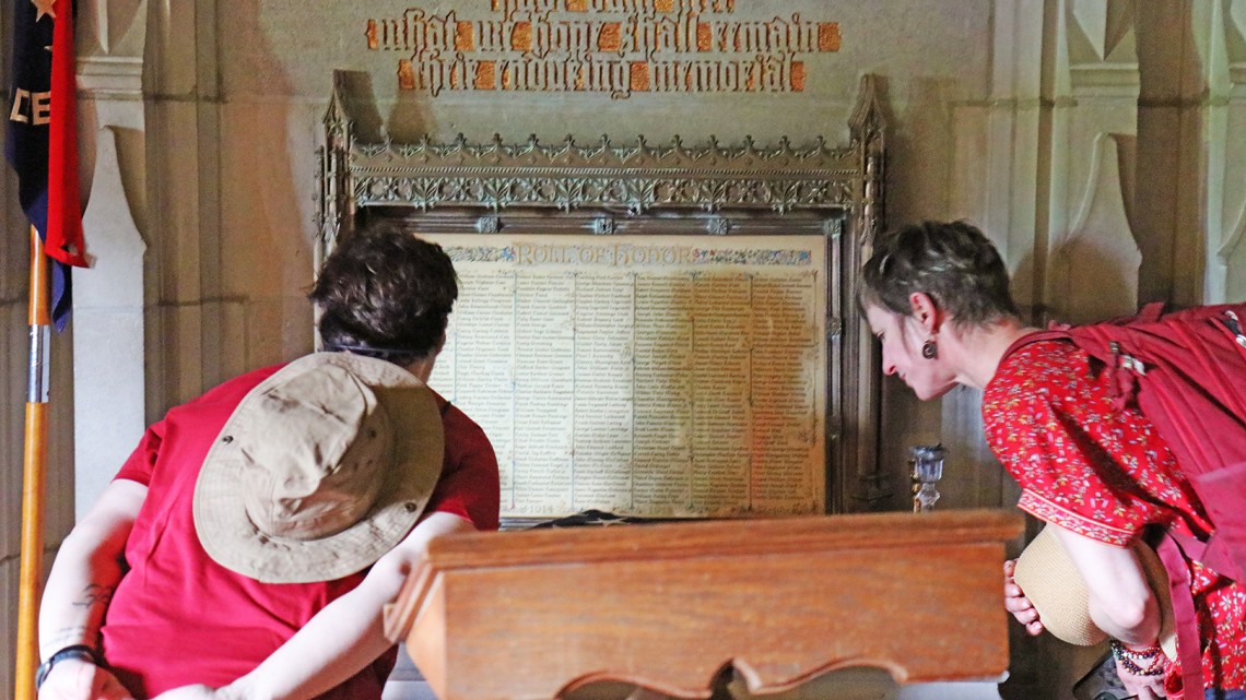 two people peering at list of names on vintage campus memorial