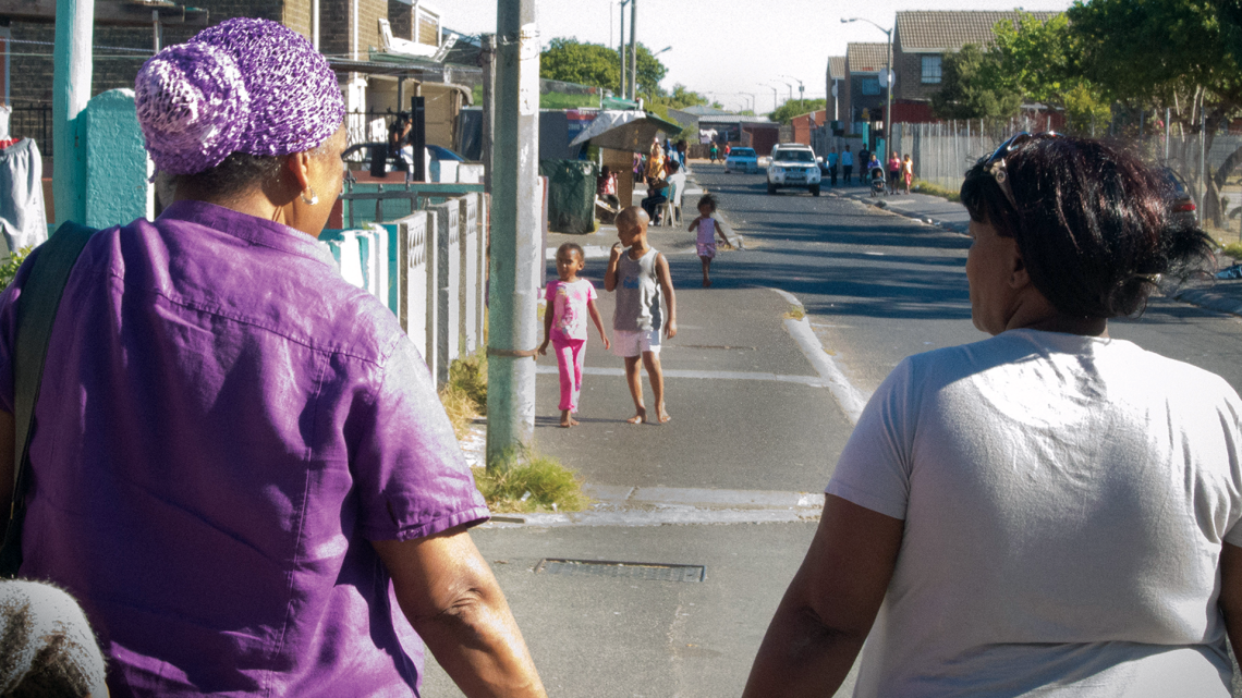 Women walking away from the camera along an urban street with children in the distance