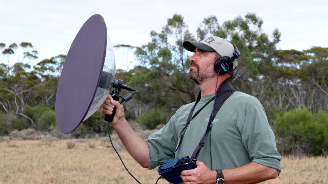 Mike Webster holding a parabolic microphone and wearing headphones