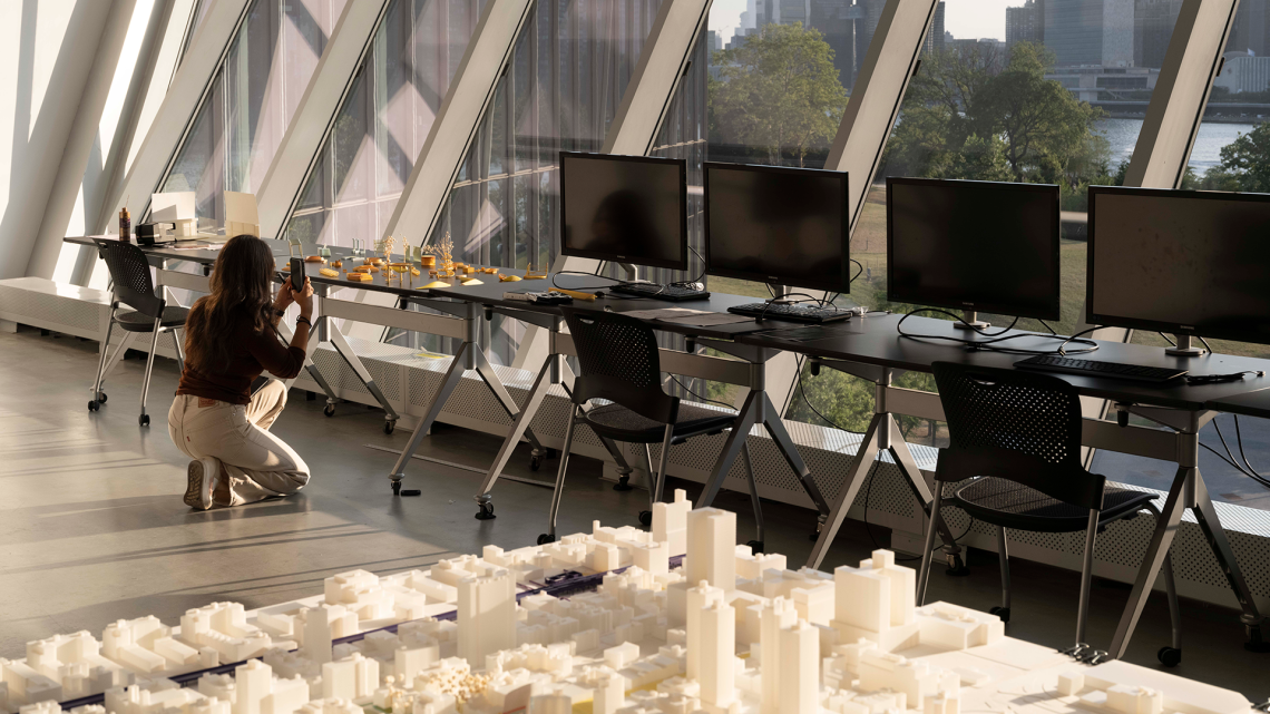 a person kneeling down taking a photo of an architectural city model on a table.