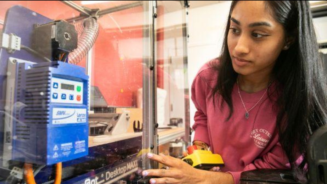 A woman leans in to work with a piece of equipment