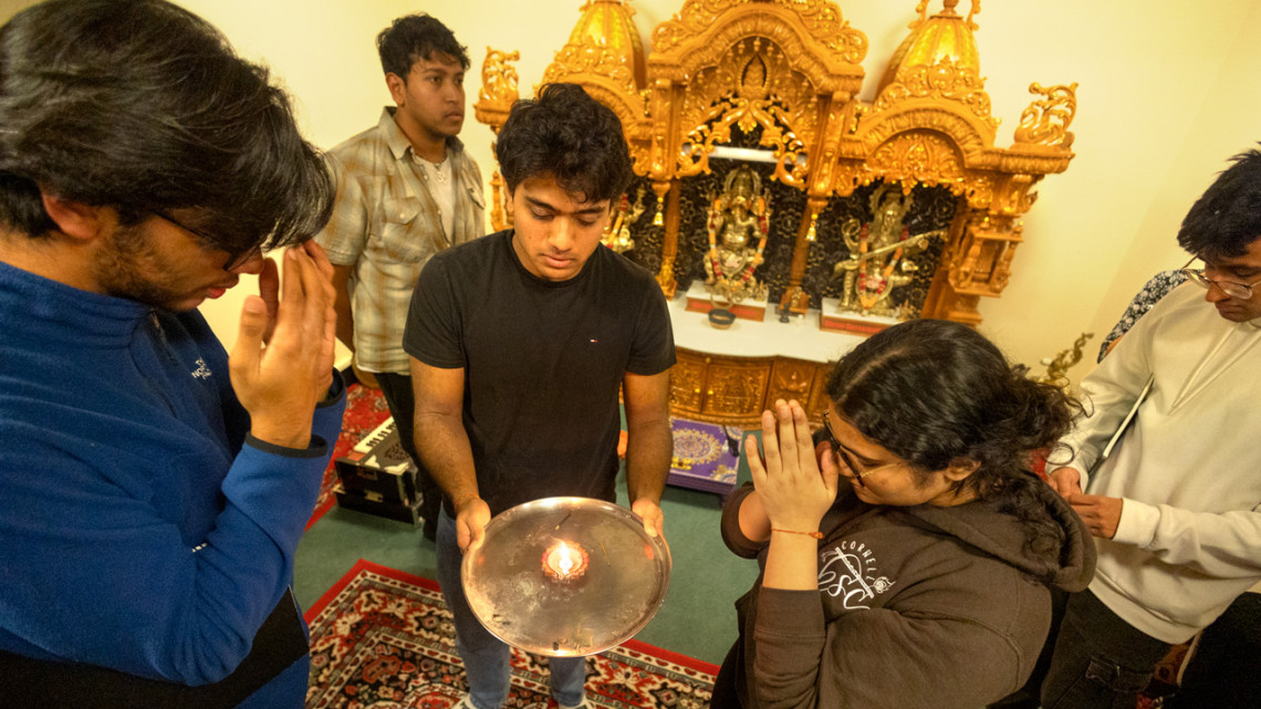 Megh Prajapati ’26, (center) former Hindu Student Council president, and Esha Shah ’27 (right), HSC’s current president, take part in blessings in the Hindu Temple room in Anabel Taylor Hall. They pass their hands over the flame and then over their heads and faces to receive sacred energy from the light of the diya.