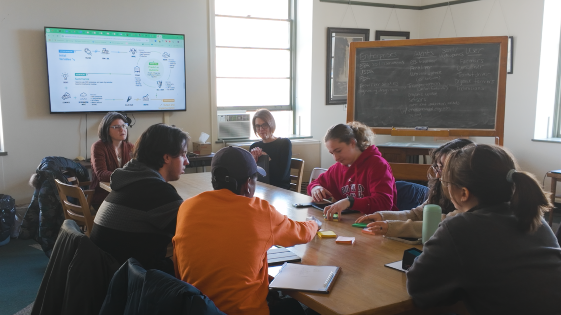 Allison Hutchison leads a group of students, seated around a table, in an activity