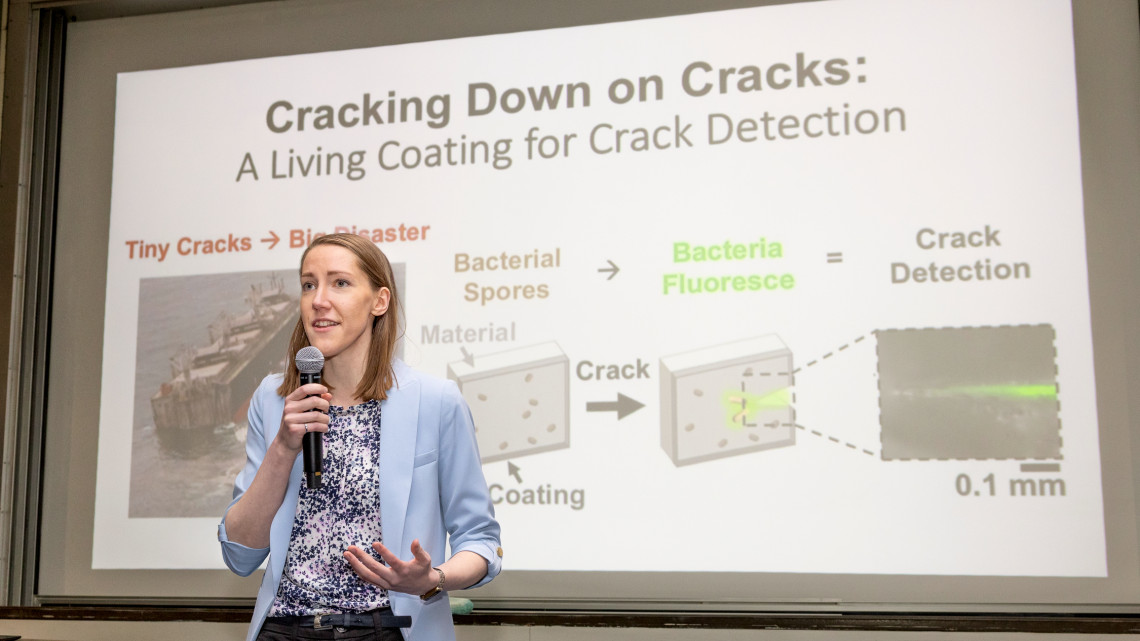 Ellen van Wijngaarden holds a microphone and presents her three minute talk while standing in front of her slide