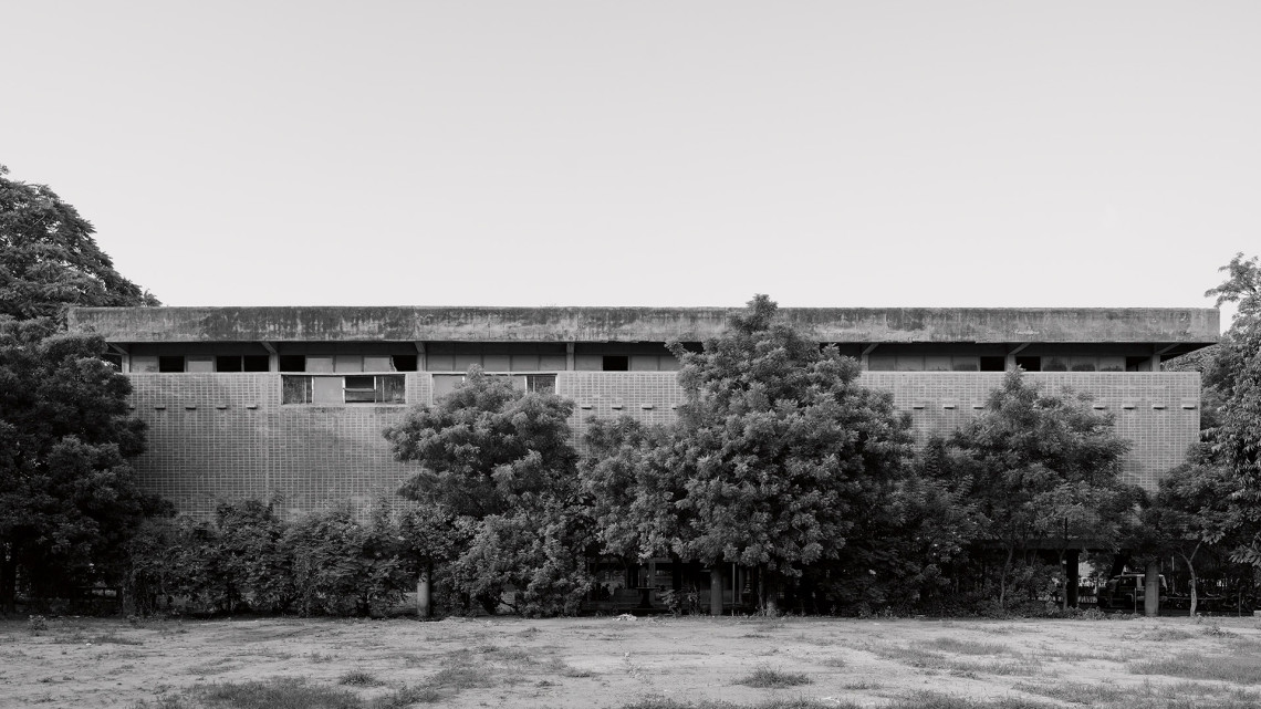 Facade of a brick building partially hidden by tree and bush foliage.