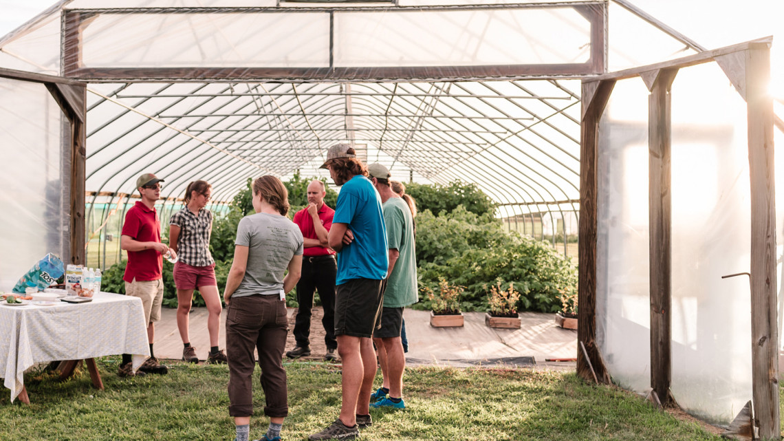 A group of people in front of a high tunnel with crops
