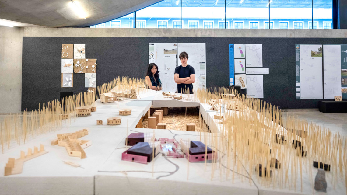 Two students view a table filled with wooden architectural models