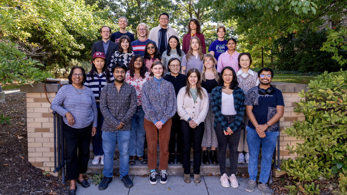 A group of 22 graduate teaching fellows stand in nature in summer.