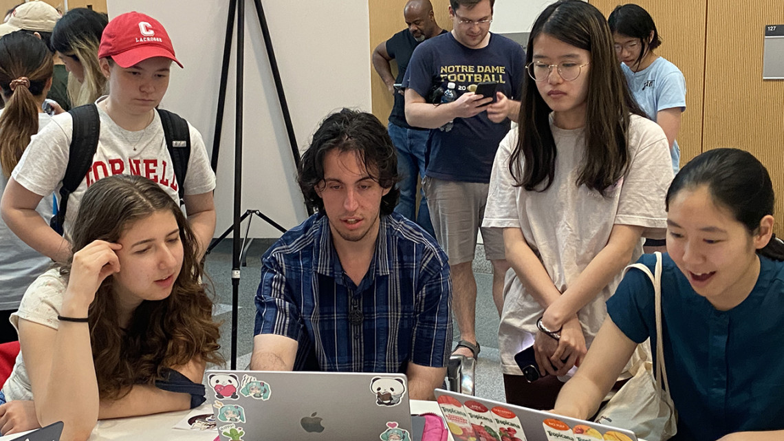 Five college students stand or sit around a table playing video games