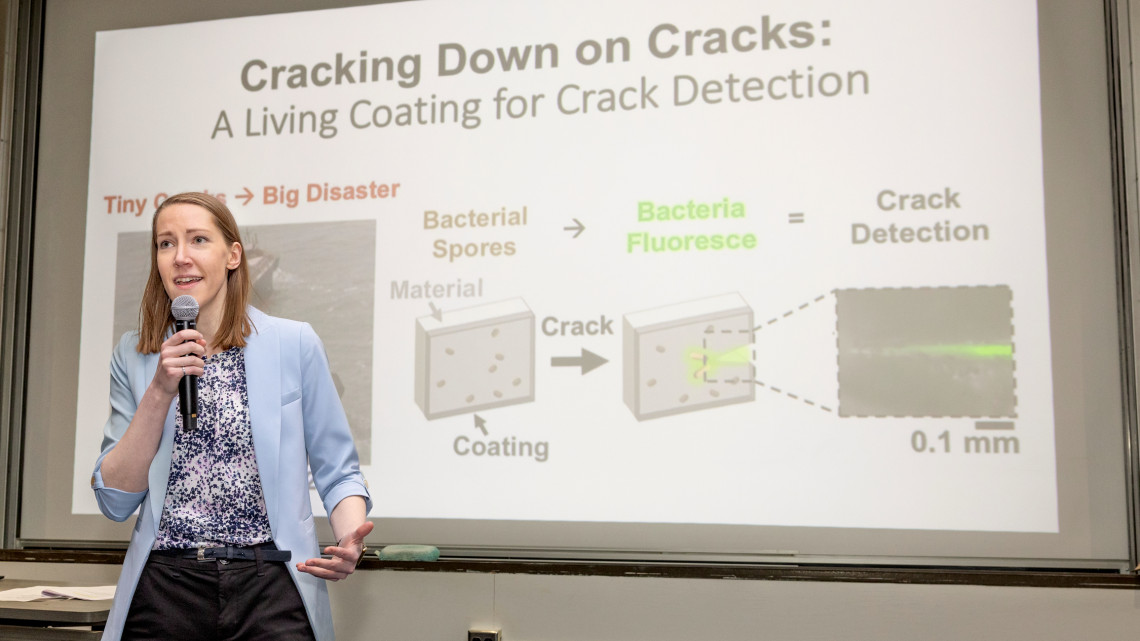 Ellen van Wijngaarden holds a microphone and presents her three minute talk while standing in front of her slide