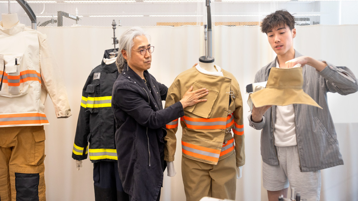 Two designers stand with fire gear they designed