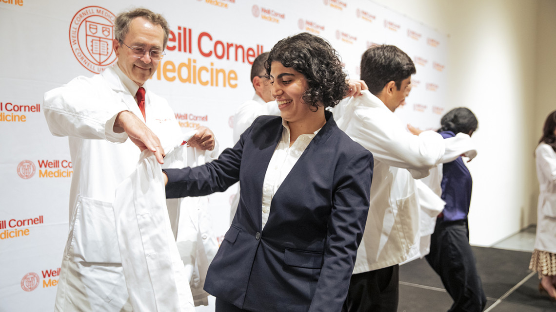 Dr. Hugh Hemmings coats medical student Hanan Akbari during the white coat ceremony.
