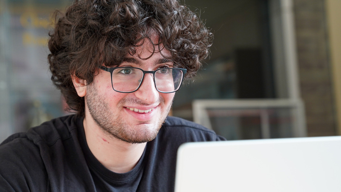 A man with curly hair and glasses smiles over a laptop screen