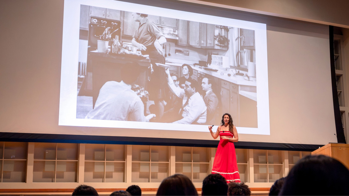Dana Beninati '15 in a red dress in front of a large screen during a presentation.