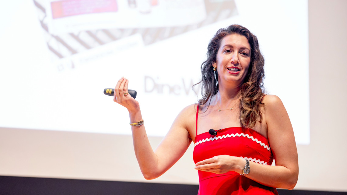 Dana Beninati '15 in a red dress in front of a large screen during a presentation.