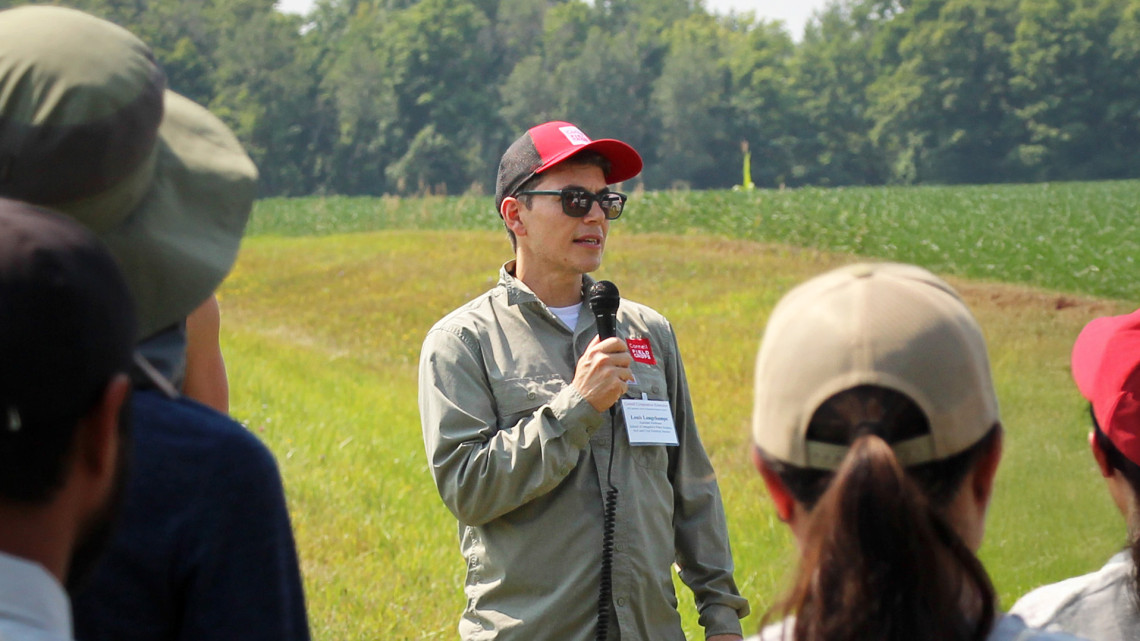 Louis Longchamps speaking to a group of people at a farm