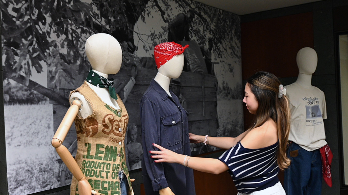 Ashlynn Potter ’28 – among a group of student collaborators – adjusts a piece from the Cornell Fashion + Textile Collection that’s part of the “Weathering the Storm” exhibit in Catherwood Library.
