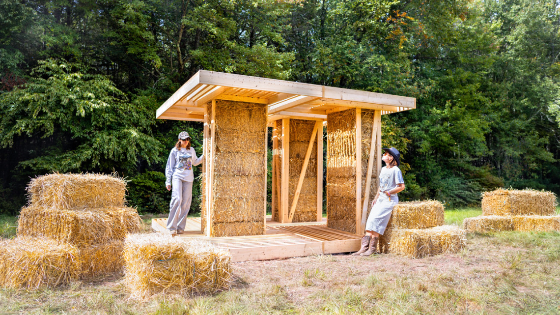 Densely packed straw bales within the interior walls of “BaleWorks,” a design-build installation by Marta Wisniewska constructed recently for BuildFest 2026 in Bethel, New York. As it evolves from a campground stage and shelter to a restroom, weathered straw will be replaced with fresh bales and repurposed for soil remediation.