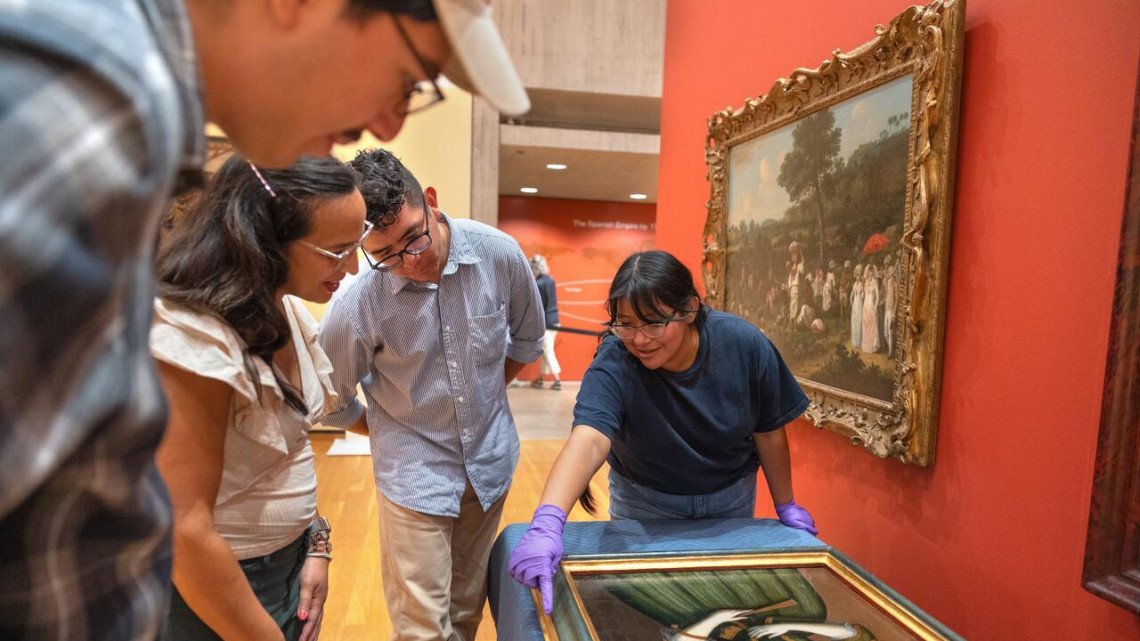 Three students gather around a portrait with a curator
